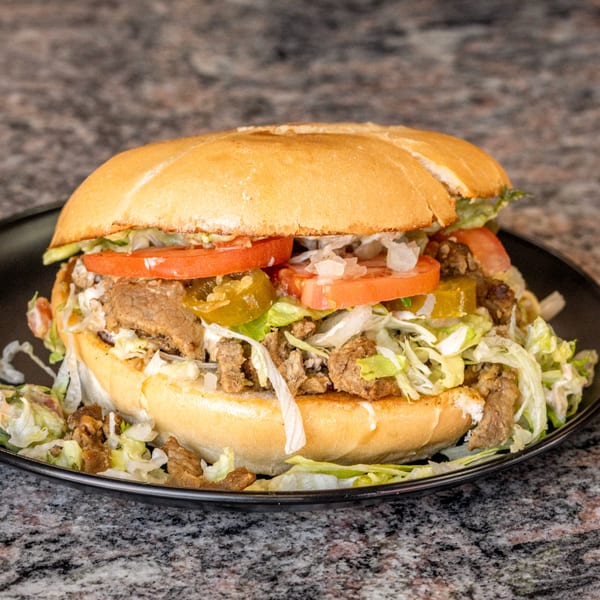 A large torta sandwich filled with meat, lettuce, tomatoes, and jalapeños on a black plate.