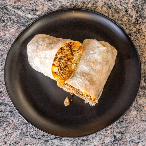 A large burrito, cut in half, revealing shredded meat and cheese, on a black plate.
