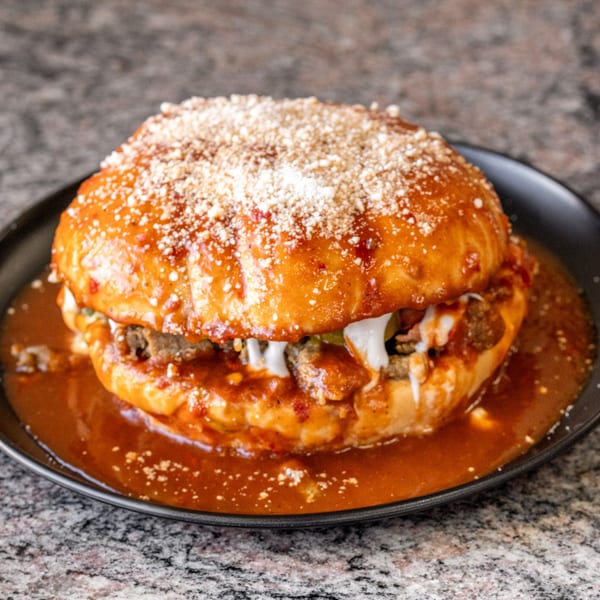 A large, saucy torta ahogada with meat, crema, and cotija cheese on a black plate.