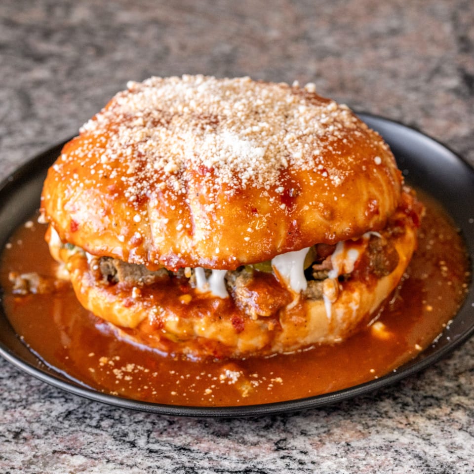 A large, saucy torta ahogada with meat, crema, and cotija cheese on a black plate.