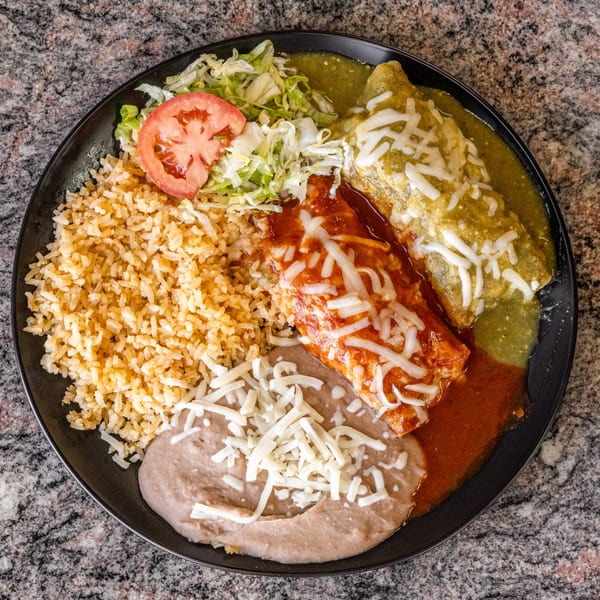A black plate of Mexican food with rice, beans, two enchiladas, lettuce, and tomato.