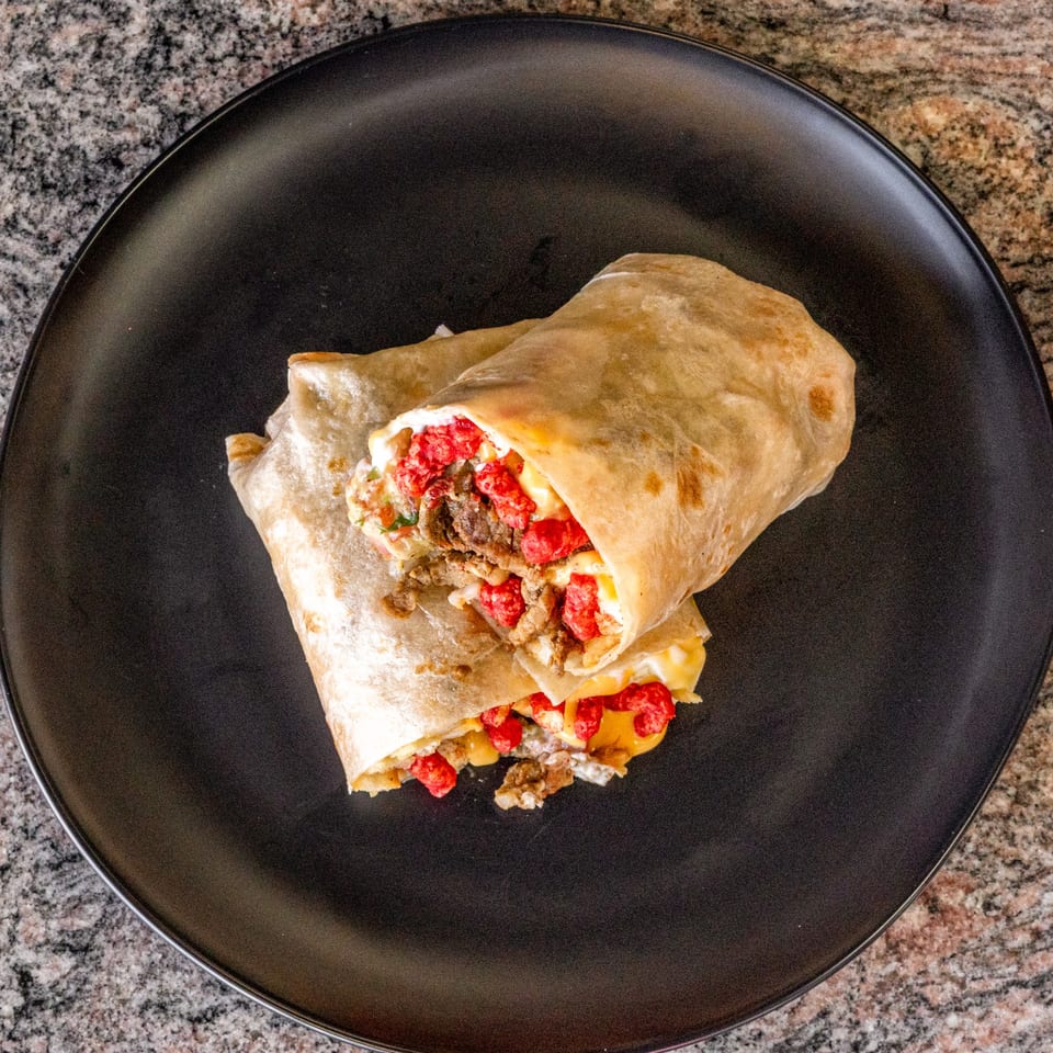 Two halves of a burrito filled with meat, cheese, and red crunchy toppings on a black plate.